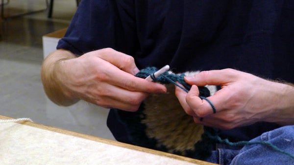 An inmate crochets a scarf at the Oregon State Correctional Institution as part of “Crocheting 4 Community.” The group of about twenty men meet four nights a week to crochet and work in hobby crafts, which they donate to charitable causes. Photo by Ricci Cande.