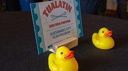 Photograph of Tualatin kick off. Shows a close up of a designed card with the city name and the Sustainable City Year Program name with two toy ducks in front.