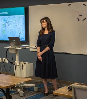 Femme presenting person in a dress talks about their MCRP project to a class.