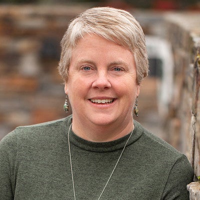 Photograph of a woman with cropped hair in front of a blurred object. 