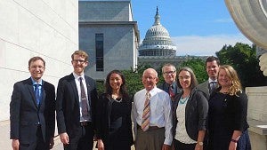 group poses for photo in business attire with capitol building in background